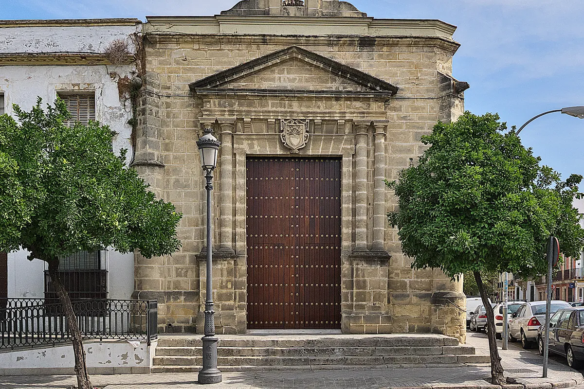 The stone front of the Chapel of Angustias in Jerez, a small chapel with a bell gable, a carved doorway and orange trees in front of it
