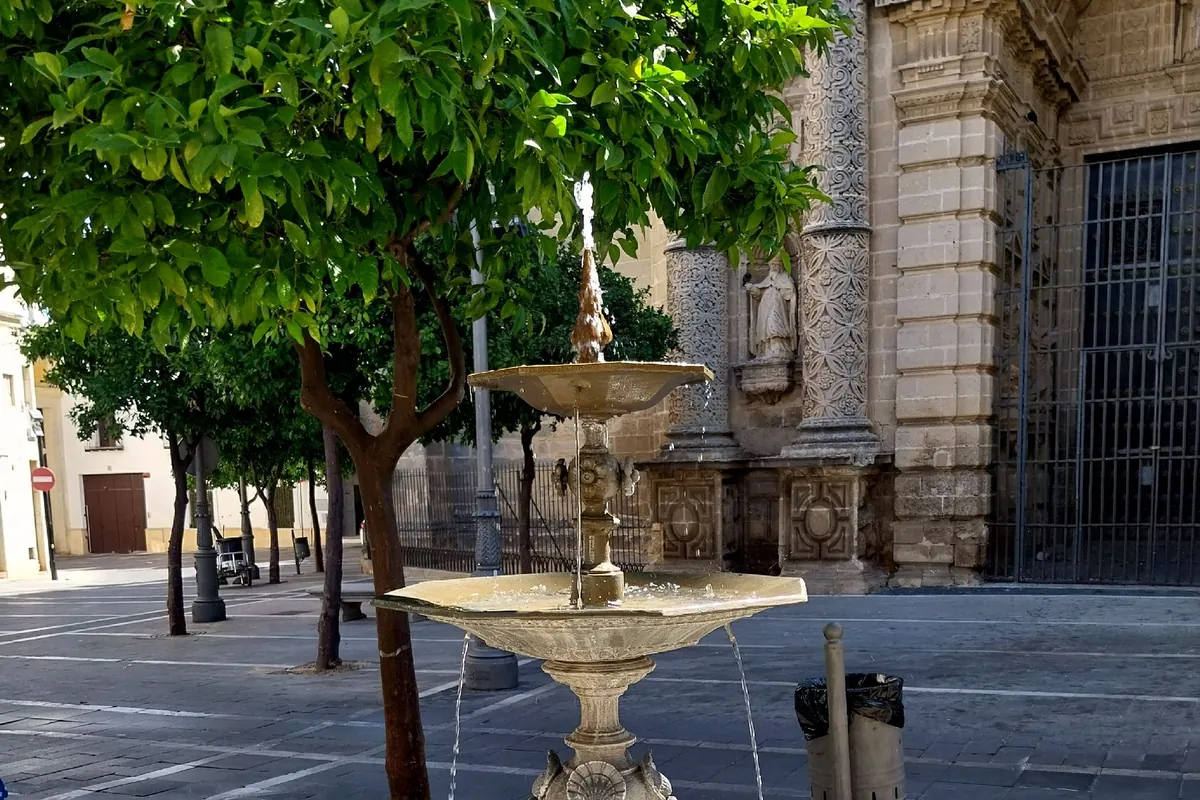 A stone fountain with a carved basin in the Plaza de San Miguel in Jerez, with orange trees and the doorway of the church behind it