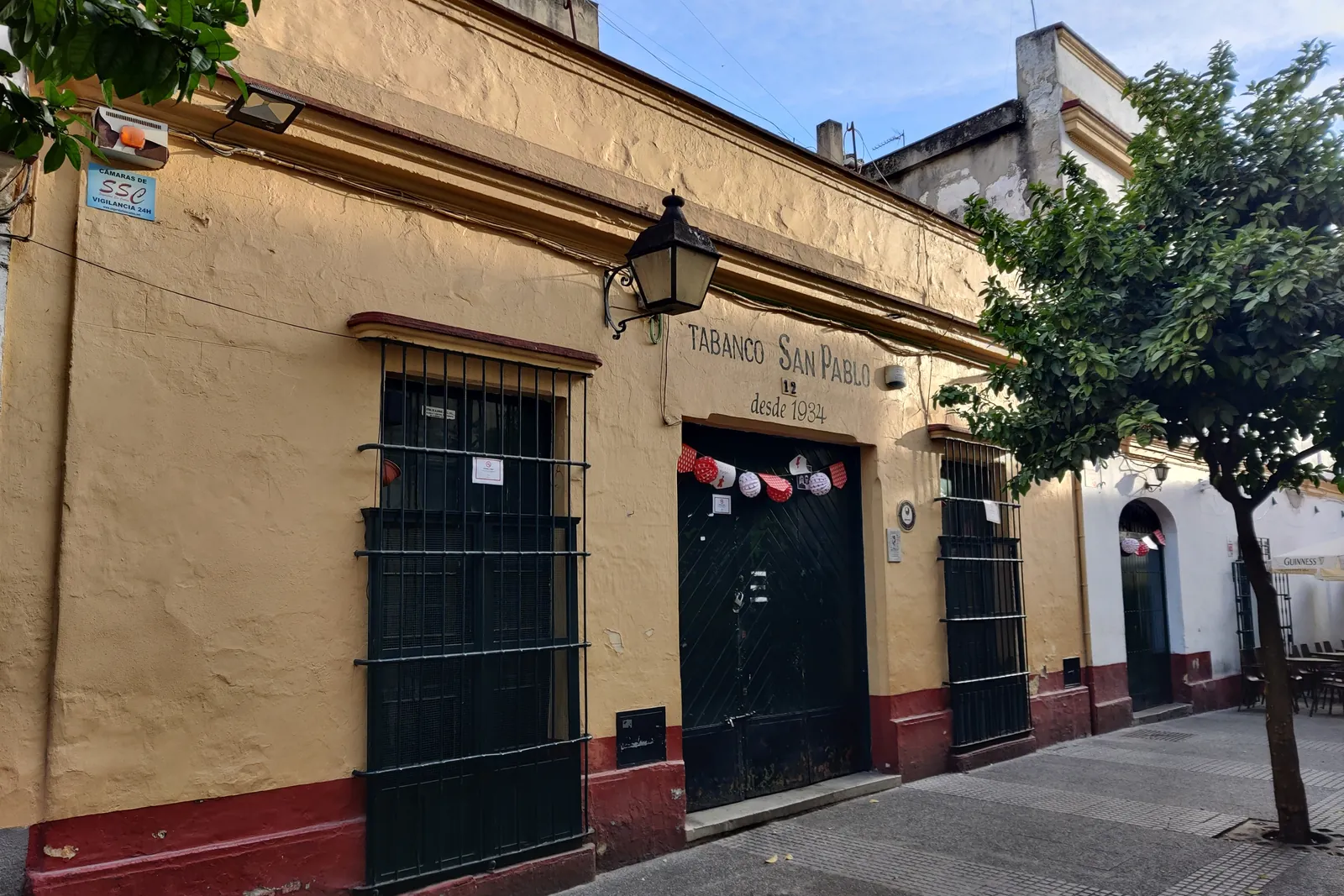 The ochre front of a tabanco in Jerez, with barred windows, a street lantern and orange trees beside it
